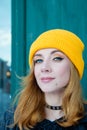 Beautiful young woman with blonde hair and blue eyes in a yellow knitting hat on a background of green wall. Royalty Free Stock Photo