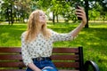 Beautiful young woman with blonde hair taking selfie at the city park. Girl sitting on a bench in a sunny day. Active life concept Royalty Free Stock Photo