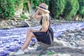 A beautiful young woman blonde with long hair in a hat sitting on a rocky shore by the river. Around the mountains Royalty Free Stock Photo