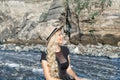 A beautiful young woman blonde with long hair in a hat sitting on a rocky shore by the river. Around the mountains Royalty Free Stock Photo