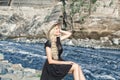 A beautiful young woman blonde with long hair in a hat sitting on a rocky shore by the river. Around the mountains Royalty Free Stock Photo