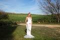 A beautiful young woman, blonde and with long hair, wearing a white dress and a crown of flowers in her hair, is in a field. In Royalty Free Stock Photo