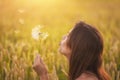 Beautiful young woman blows dandelion in a wheat field in the summer sunset. Beauty and summer concept