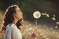 Beautiful young woman blows dandelion in a wheat field in the summer sunset. Beauty and summer concept Royalty Free Stock Photo