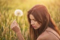 Beautiful young woman blows dandelion in a wheat field in the summer sunset. Beauty and summer concept Royalty Free Stock Photo