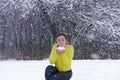 Beautiful young woman blows snow from hands in winter forest. Powder snowflakes fly up. Joyful lady in bright yellow jacket Royalty Free Stock Photo