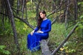 Beautiful, young woman in a blue dress is sitting on a fallen tree in the background of a forest and dry twigs. Royalty Free Stock Photo