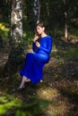 Beautiful, young woman in a blue dress is sitting near a tree over a cliff, against a forest background. Royalty Free Stock Photo