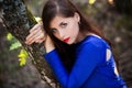 Beautiful, young woman in a blue dress is sitting near a tree over a cliff, against a forest background. Royalty Free Stock Photo