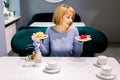 Beautiful young woman in blue sweater is having tea and cake in a nice cafe. Woman choosing between red and yellow tasty Royalty Free Stock Photo