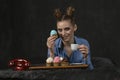 Beautiful young woman with bright makeup and bun hairstyle drinks coffee with muffins decorated with multicolored cream