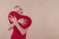 Beautiful young woman in a bright red slinky dress hugging a plush heart Royalty Free Stock Photo