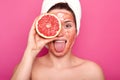 Beautiful young woman with bright scrub on her face holds half of rape grapefruit in one hand, sticks out her tongue, having white Royalty Free Stock Photo