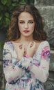 beautiful young woman with brown hair, red lips standing on stone wall background obletennoy branches in white and purple dress Royalty Free Stock Photo