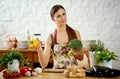 Beautiful young woman holds broccoli and yellow peppers in the kitchen at a table full of vegetables