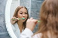 A beautiful young woman brushes her teeth and looks in the mirror Royalty Free Stock Photo