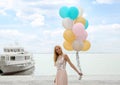 Beautiful young woman with bunch of balloons near sightseeing boat