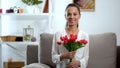 Beautiful young woman with bunch of tulips sitting on sofa and smiling at camera Royalty Free Stock Photo