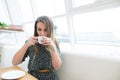 Beautiful young woman in a cafe holding a cup of tea, seen through the window with buildings and lights reflections. Royalty Free Stock Photo