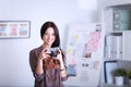 Beautiful young woman with camera standing near desl in office