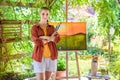 Beautiful young woman, a cancer survivor, posing in front of her art canvas painting outdoors in her garden.