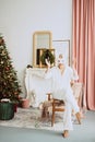 Beautiful young woman in a carnival rabbit mask and white costume celebrates the new year near the Christmas tree in a modern Royalty Free Stock Photo