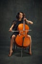 Beautiful Young Woman, Cellist Sitting With Cello On Vintage Green Background. Magazine Cover About Talented Musicians