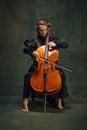 Beautiful young woman, cellist sitting on chair and playing cello against vintage green background. Classic music Royalty Free Stock Photo