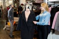 Beautiful young woman chooses a black coat in a clothing store. A man with a beard looks at her Royalty Free Stock Photo