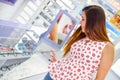 Beautiful young woman choosing a glasses in optical store inside of showcase in a blurred background