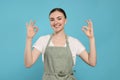 Beautiful young woman in clean apron with pattern on light blue background Royalty Free Stock Photo