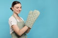 Beautiful young woman in clean apron with pattern and oven glove on light blue background. Space for text Royalty Free Stock Photo