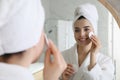 Beautiful young woman cleaning her face with cotton disk near mirror in bathroom Royalty Free Stock Photo