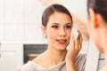 Close up over the shoulder view of young woman cleaning her face with a cotton pad in the evening in her bathroom Royalty Free Stock Photo