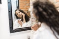 Beautiful young woman is cleaning her face using a cotton disc sponge and smiling while looking in the mirror in the bathroom Royalty Free Stock Photo