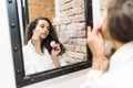 Beautiful young woman is cleaning her face using a cotton disc sponge and smiling while looking in the mirror in the bathroom Royalty Free Stock Photo