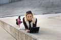 Beautiful young woman close up. Blonde girl is sitting on steps outside an office, holding a tablet. Female with notebook. Royalty Free Stock Photo