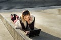 Beautiful young woman close up. Blonde girl is sitting on steps outside an office, holding a tablet. Female with notebook. Royalty Free Stock Photo