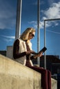 Beautiful young woman close up. Blonde girl is sitting on steps outside an office, holding a tablet. Female with notebook. Royalty Free Stock Photo