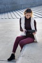 Beautiful young woman close up. Blonde girl is sitting on steps outside an office, holding a tablet. Female with notebook. Royalty Free Stock Photo