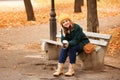 Beautiful young woman with coffee resting on wooden bench in autumn park Royalty Free Stock Photo