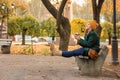 Beautiful young woman with coffee resting on wooden bench in autumn park Royalty Free Stock Photo