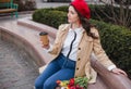 Beautiful young woman with coffee to go and spring tulips flowers bouquet at city street. Happy girl walking outdoors. Spring Royalty Free Stock Photo