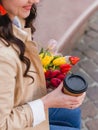 Beautiful young woman with coffee to go and spring tulips flowers bouquet at city street. Happy girl walking outdoors. Spring Royalty Free Stock Photo