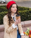 Beautiful young woman with coffee to go and spring tulips flowers bouquet at city street. Happy girl walking outdoors. Spring Royalty Free Stock Photo