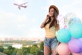 Beautiful young woman with color balloons under sky with flying airplane Royalty Free Stock Photo