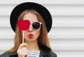 Beautiful young woman covering her eyes with red heart shaped lollipop blowing red lips sending sweet air kiss on a Royalty Free Stock Photo