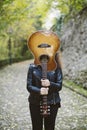 Beautiful young woman covering her face with a guitar. Royalty Free Stock Photo