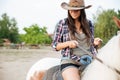 Beautiful young woman cowgirl sitting and riding horse in village