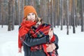 Beautiful young woman is cuddling little dog wrapped in red checkered plaid on a walk in winter forest Royalty Free Stock Photo